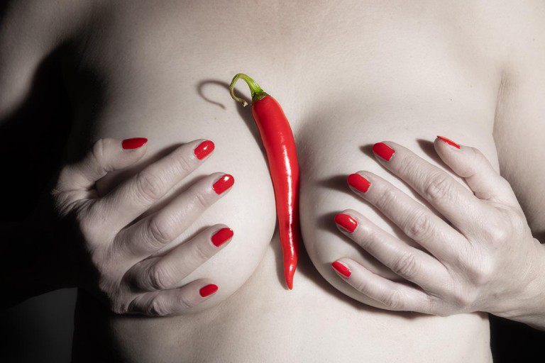 Rote Peperoni und Fingernägel auf nacktem Frauenoberkörper Sättigung reduziert