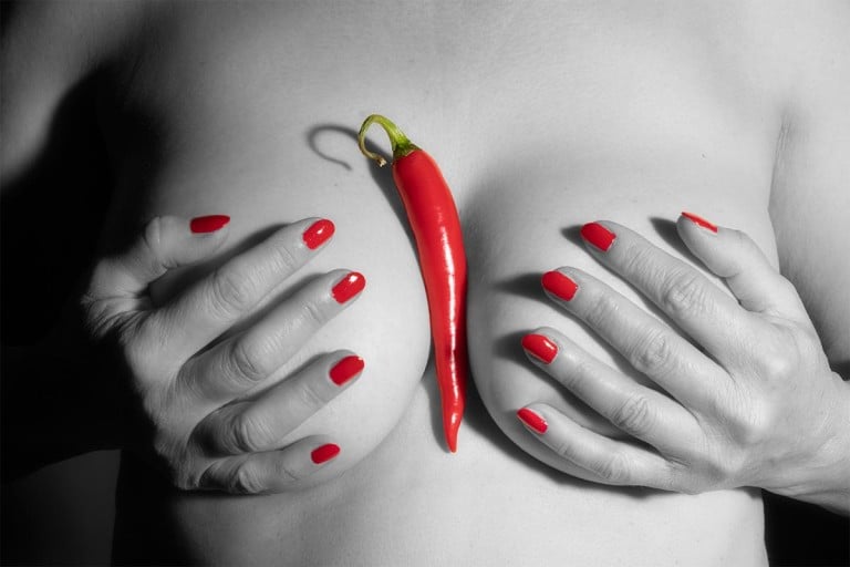 Rote Peperoni und Fingernägel auf nacktem Frauenoberkörper in sw