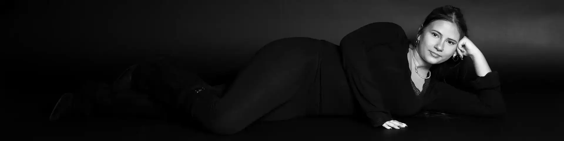 junge Frau liegend in schwarzwei&szlig; Bild, dunkler Kleidung vor einem Schwarzen Hintergrund