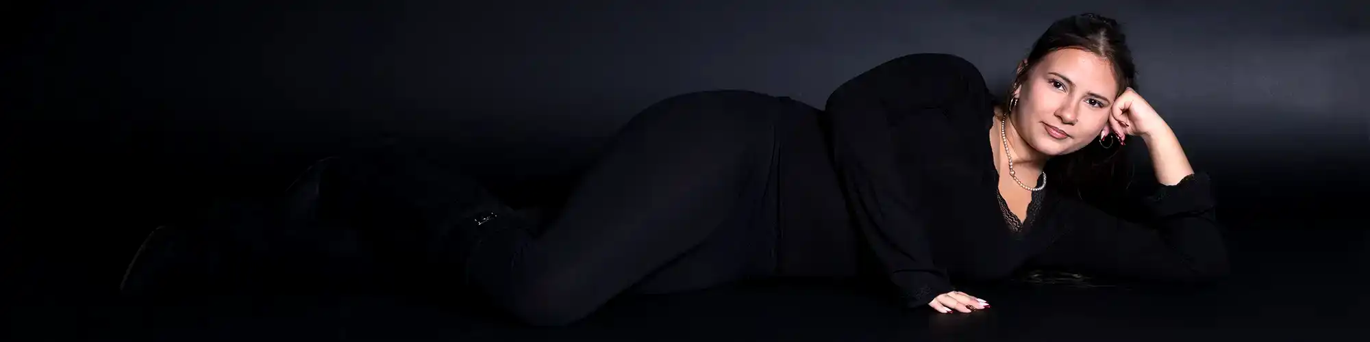 junge Frau liegend in dunkler Kleidung vor einem Schwarzen Hintergrund